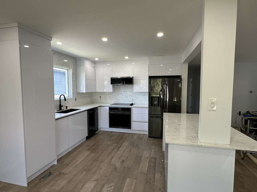 Gloss white handleless kitchen with black appliances and quartz peninsula, by Limakdéco