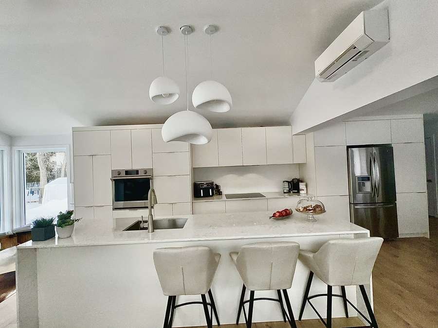 Handleless white kitchen with quartz peninsula and globe pendant lights, by Limakdéco